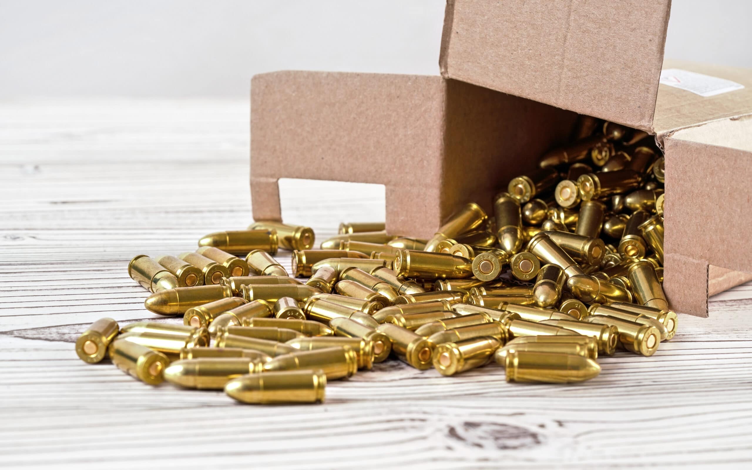 Yellow brass gun ammo spilled from paper carton box on white boar desk - close up